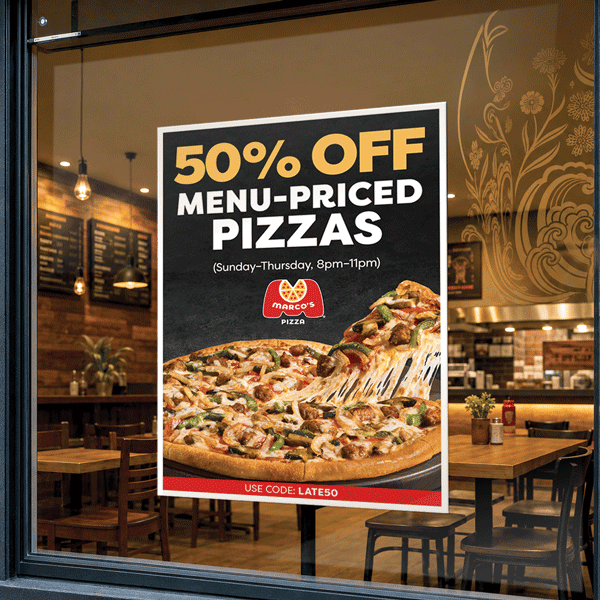 Poster on a restaurant window advertising 50% off menu-priced pizzas, valid Sunday–Thursday 8pm–11pm. Marco’s Pizza logo above an image of a large cheesy pizza with a slice being lifted. Bottom text reads “Use code: LATE50,” with a warm dining space behind.